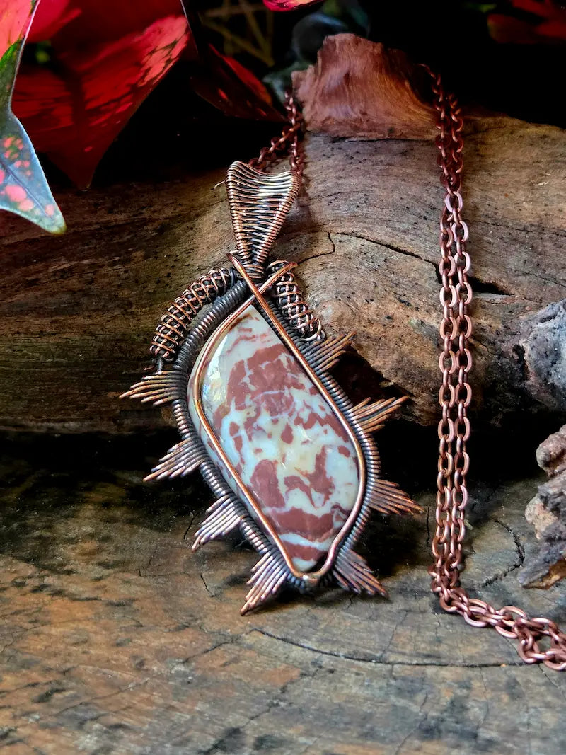 Copper wire-wrapped pendant with a natural stone on a wooden surface