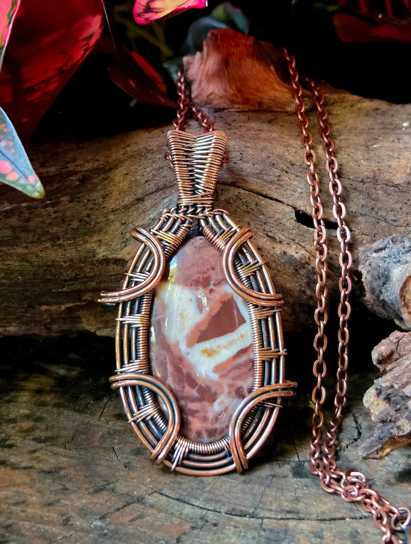 Copper-wrapped pendant with a stone on a wooden surface