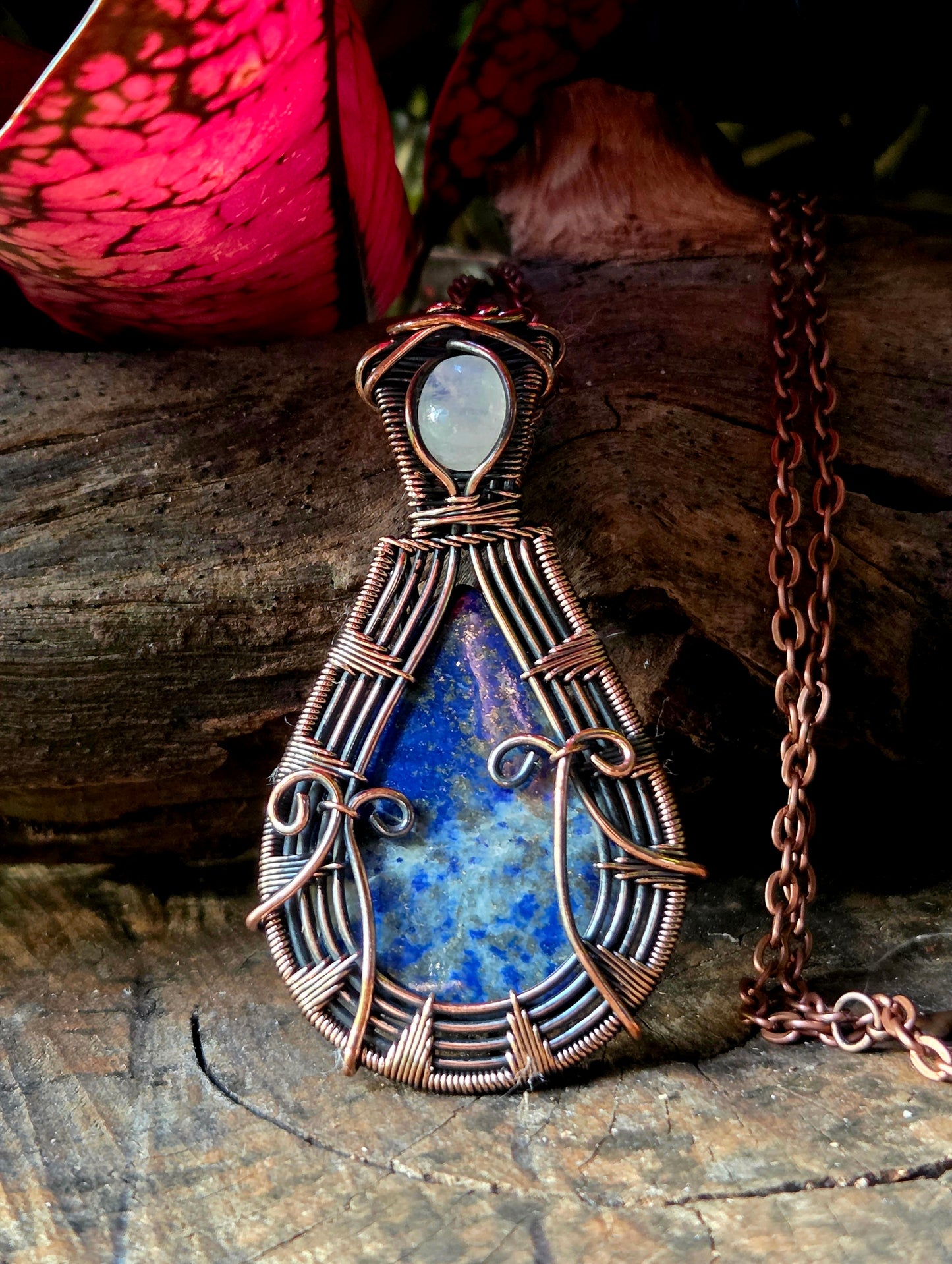Copper pendant necklace on a natural wooden surface with red leaves in the background 