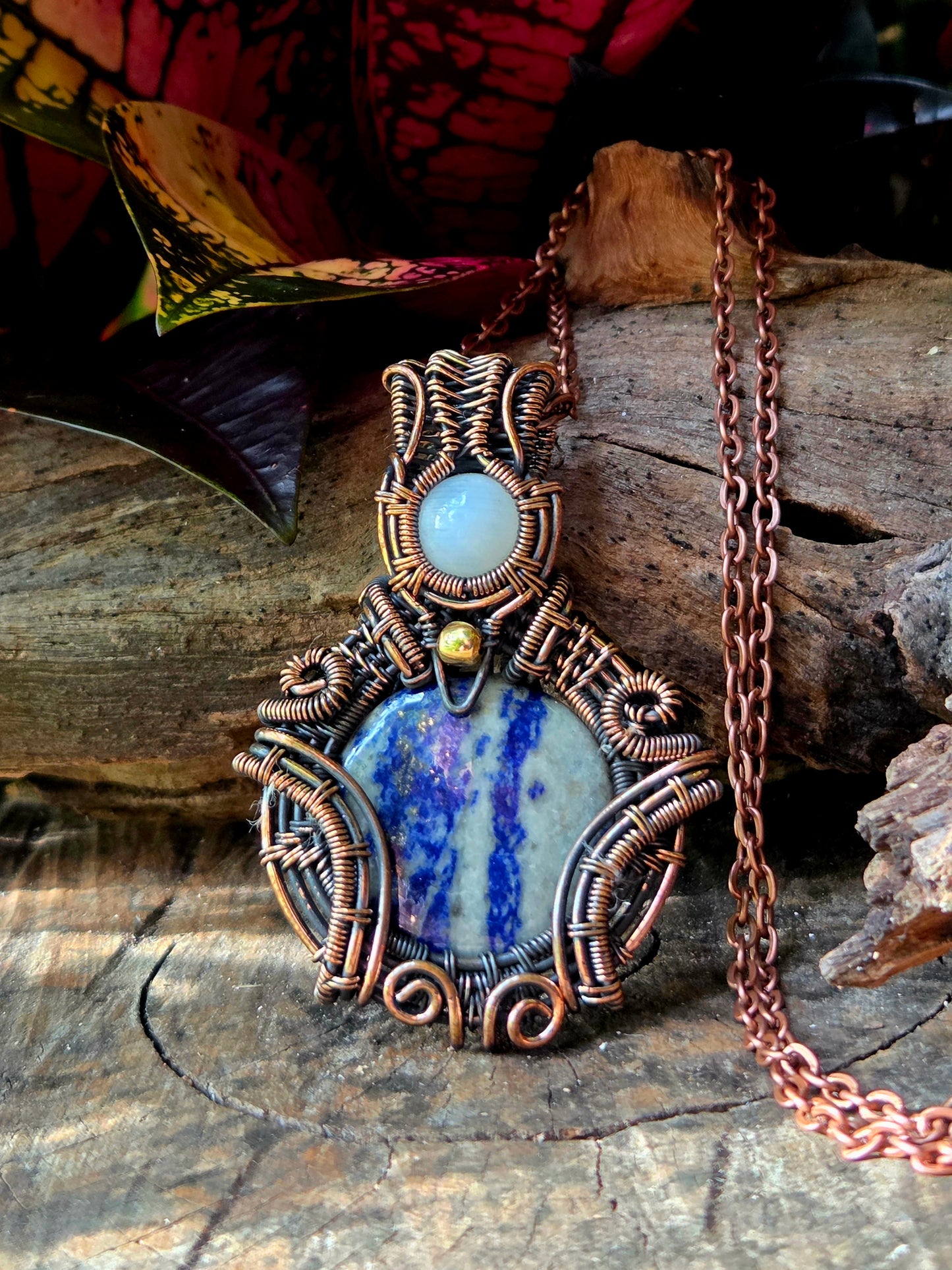 Lapis Lazuli Copper Wire Wrapped Pendant Necklace on a natural wooden surface with red leaves in the background 