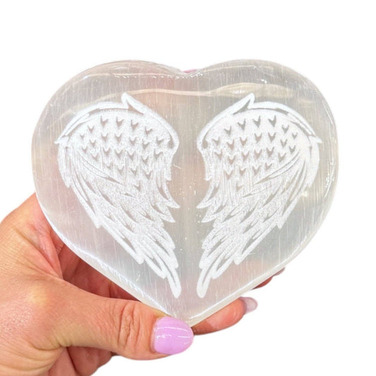 Heart-shaped selenite stone with angel wings held by a hand on a white background