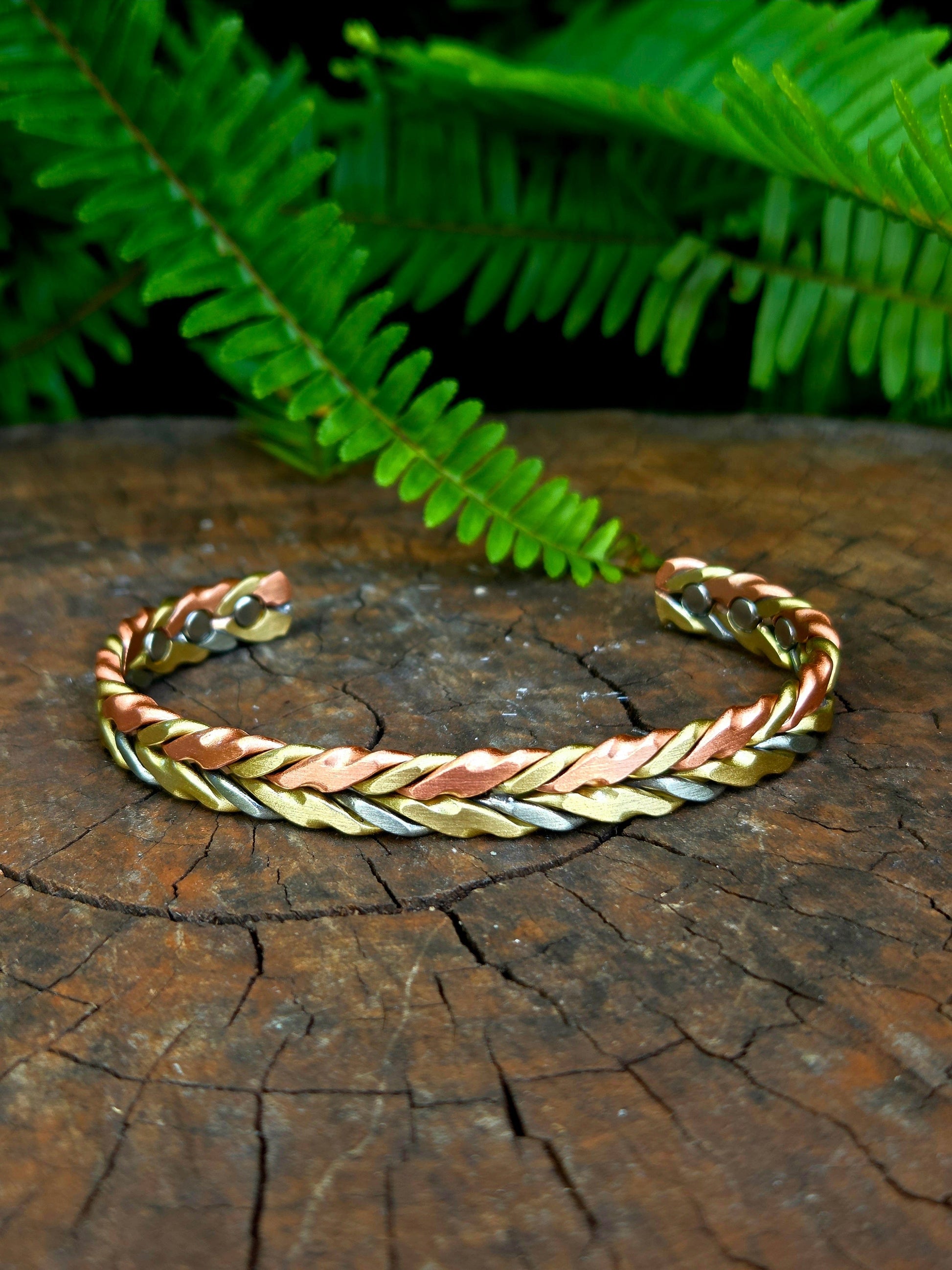Three-toned braided bracelet on a wooden surface with ferns in the background
