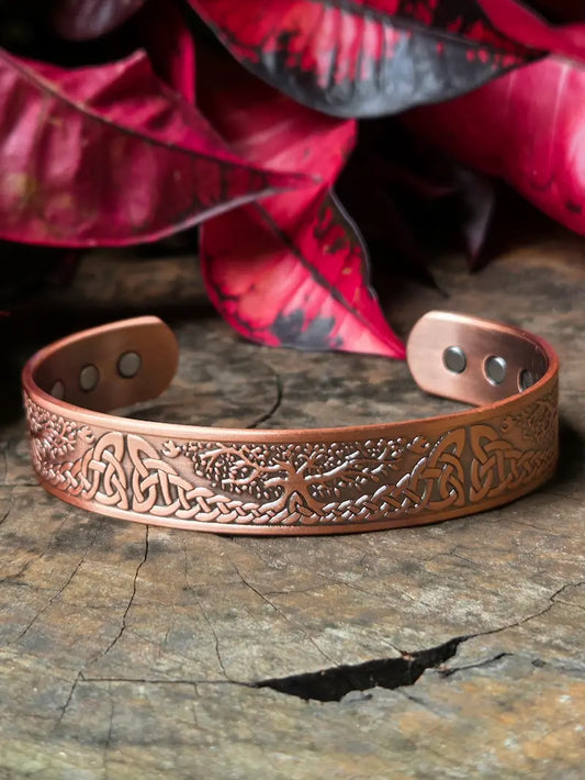 Copper bracelet with intricate designs on a wooden surface with red leaves in the background