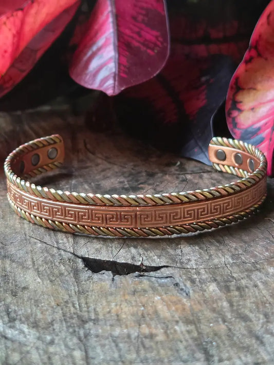 Copper bracelet with a greek design on a natural wooden surface with red leaves in the background
