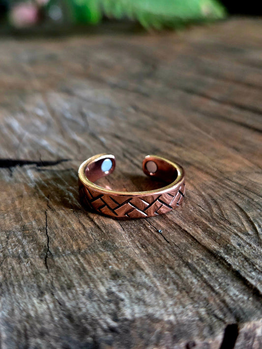 Copper ring with woven design on a wooden surface