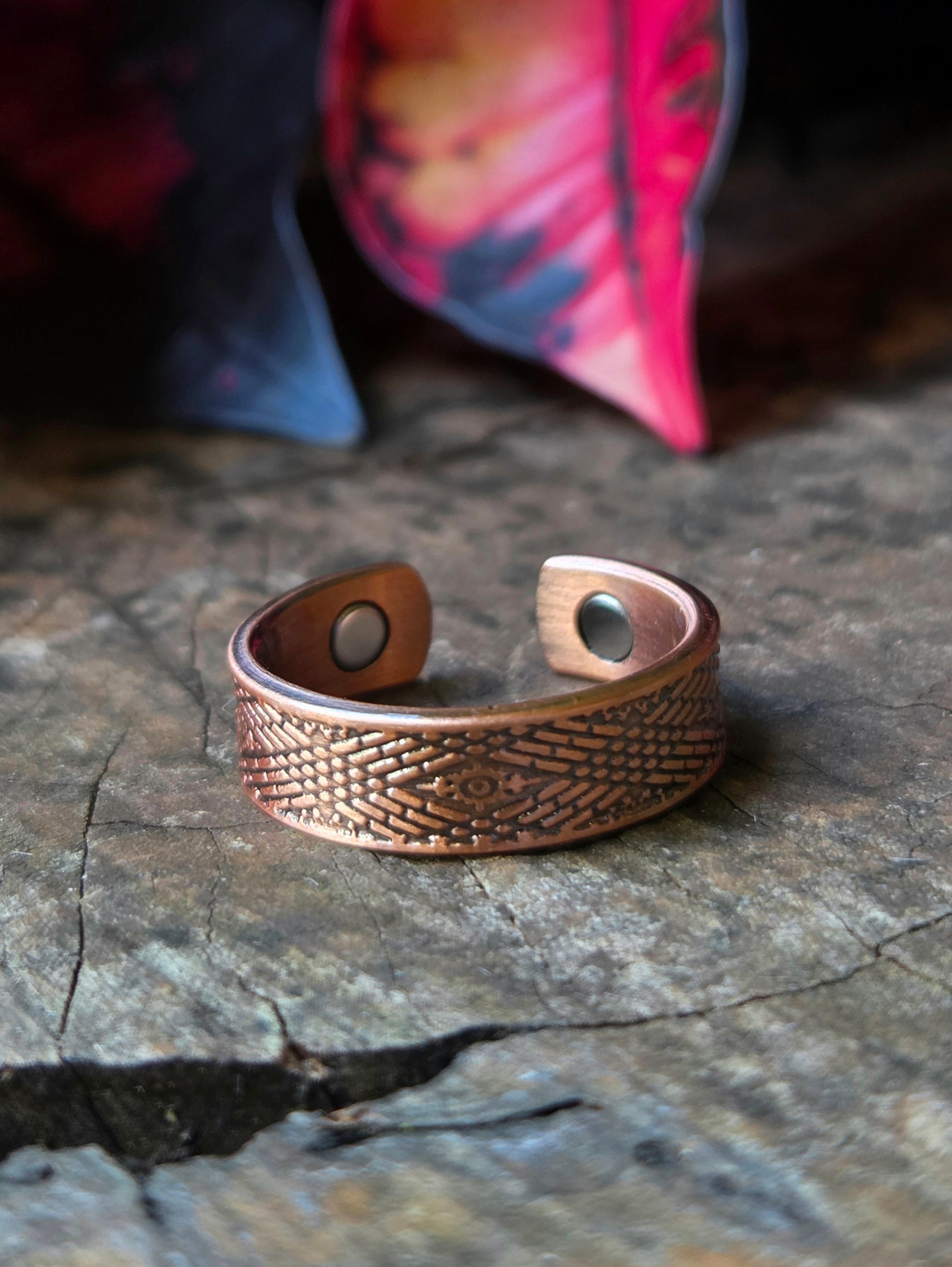 Copper ring on a natural wooden surface with red leaves in the background 