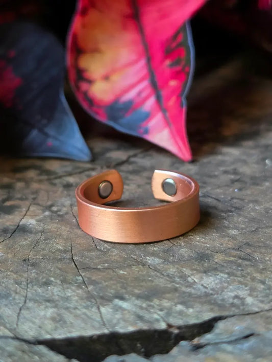 Copper ring on a textured wooden surface with red leaves in the background