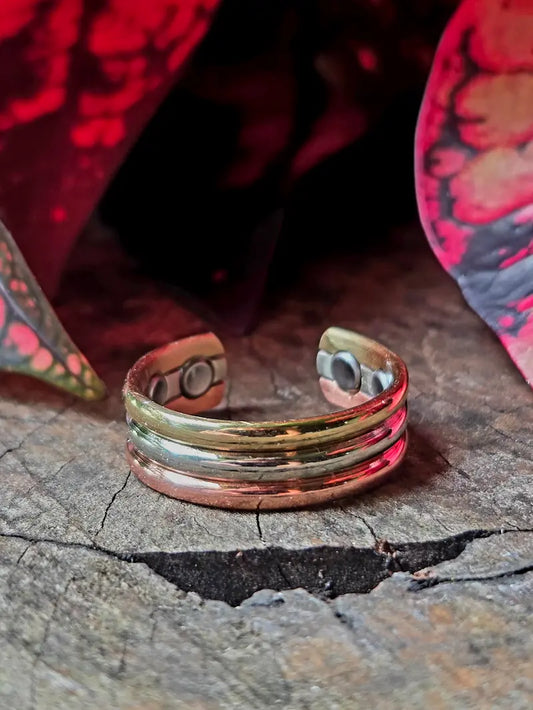 Copper Tricolour ring on a natural wooden surface with red leaves in the background 