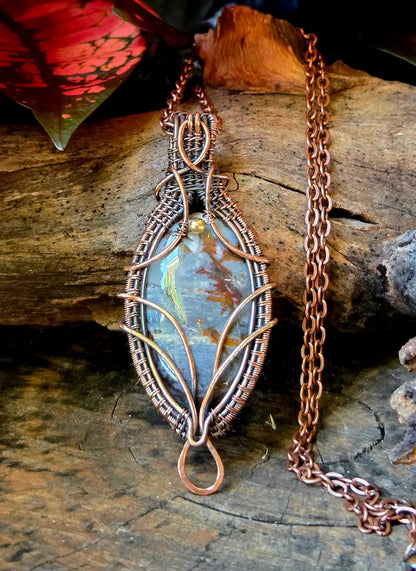 Copper wire-wrapped pendant with a blue stone on a wooden surface