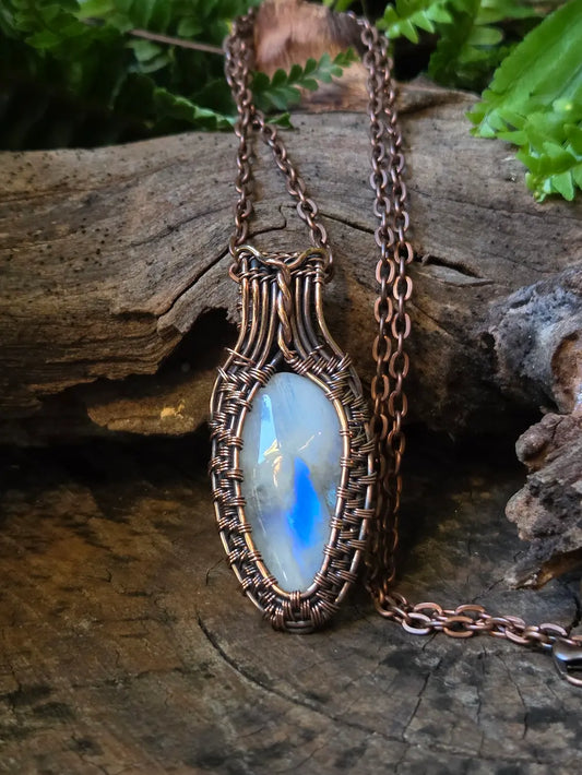 Necklace with a copper wire-wrapped pendant featuring a blue stone on a wooden surface.
