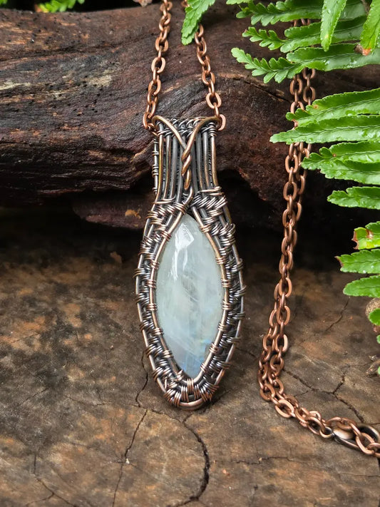 Necklace with a pendant featuring a light blue stone on a wooden surface with green leaves.