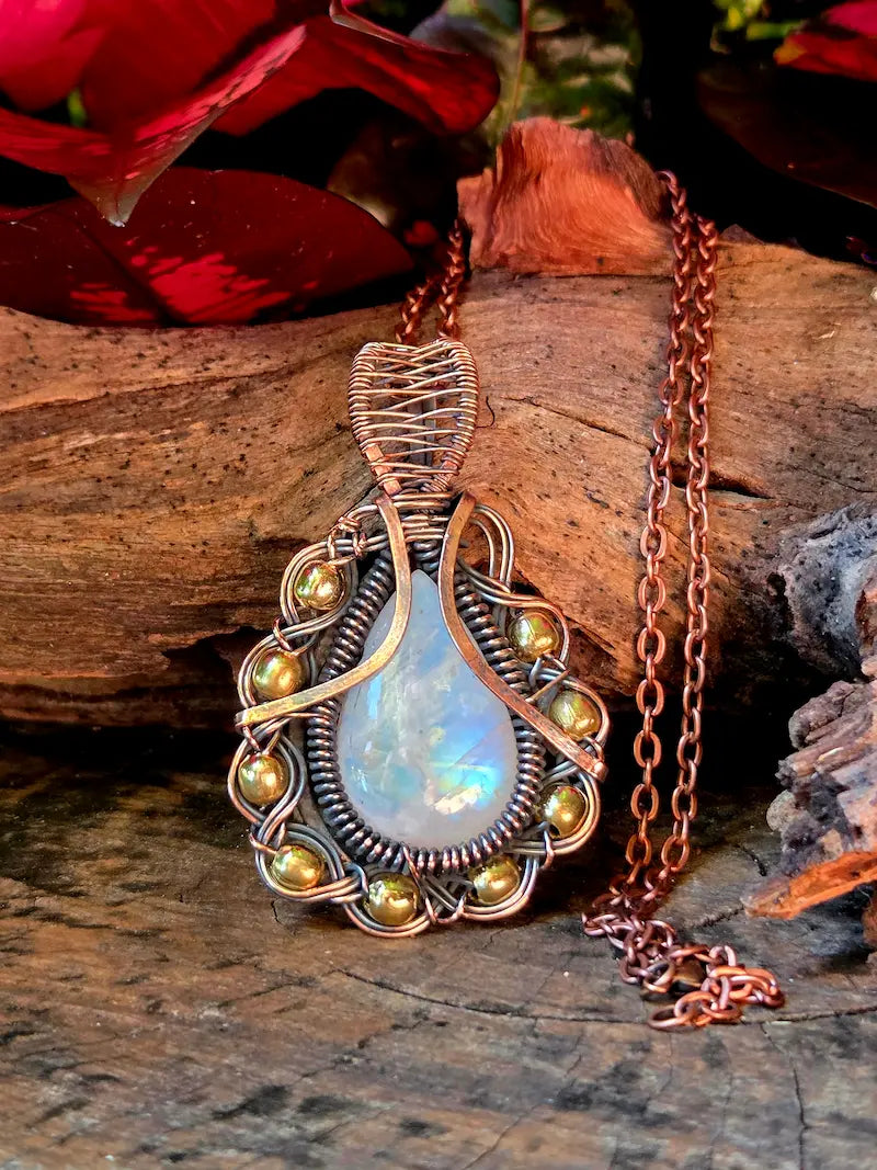 Copper wire-wrapped pendant with a teardrop-shaped moonstone gemstone on a wooden surface.
