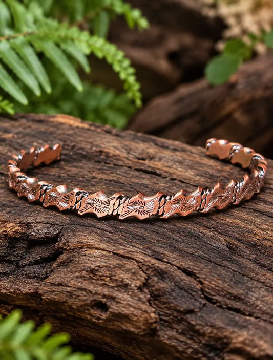 Copper bracelet with a geometric pattern on a natural wooden surface with green ferns in the background