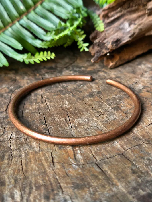 Pure copper vintage bracelet on a natural wooden surface with green ferns in the background 