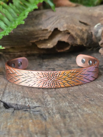 Copper bracelet on a natural wooden surface with green ferns in the background 