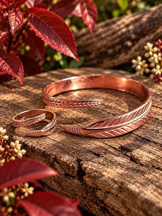 Copper bracelet with a matching ring with a feather design on a natural wooden surface with red leaves in the background 
