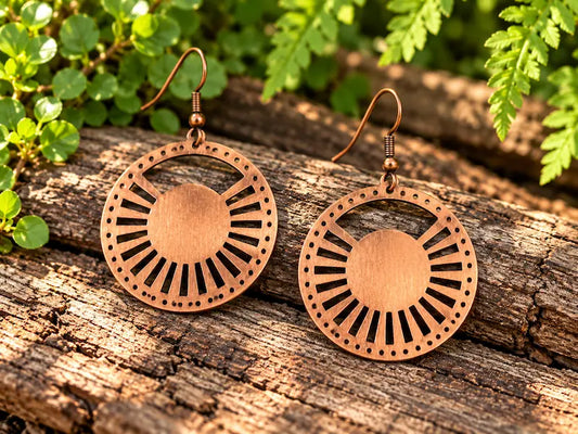 Copper Earrings with a sunburst design, resting on a natural wooden surface with green leaves in the background 