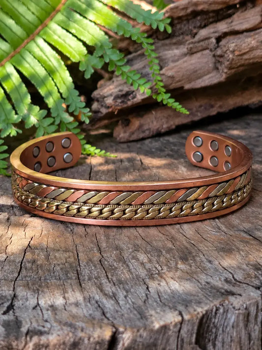 Copper bracelet with a tricolour twisted Chain-Link design, resting on a natural wooden surface with green ferns in the background.