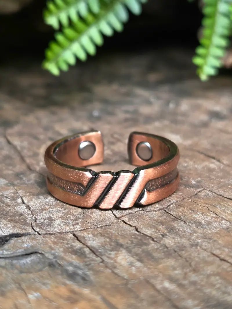Pure copper ring with Geometric pattern on natural wooden surface with green leaves in the background 