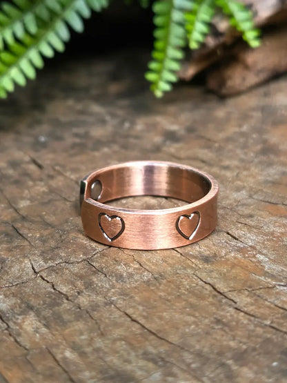 Copper ring with a love heart design on a natural wooden surface with green leaves in the background 