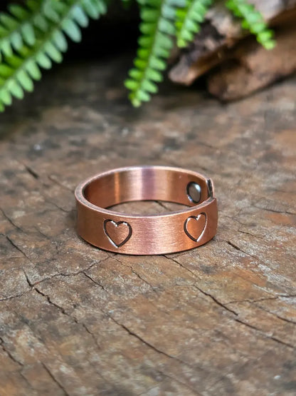 Copper ring with a love heart design on a natural wooden surface with green leaves in the background 