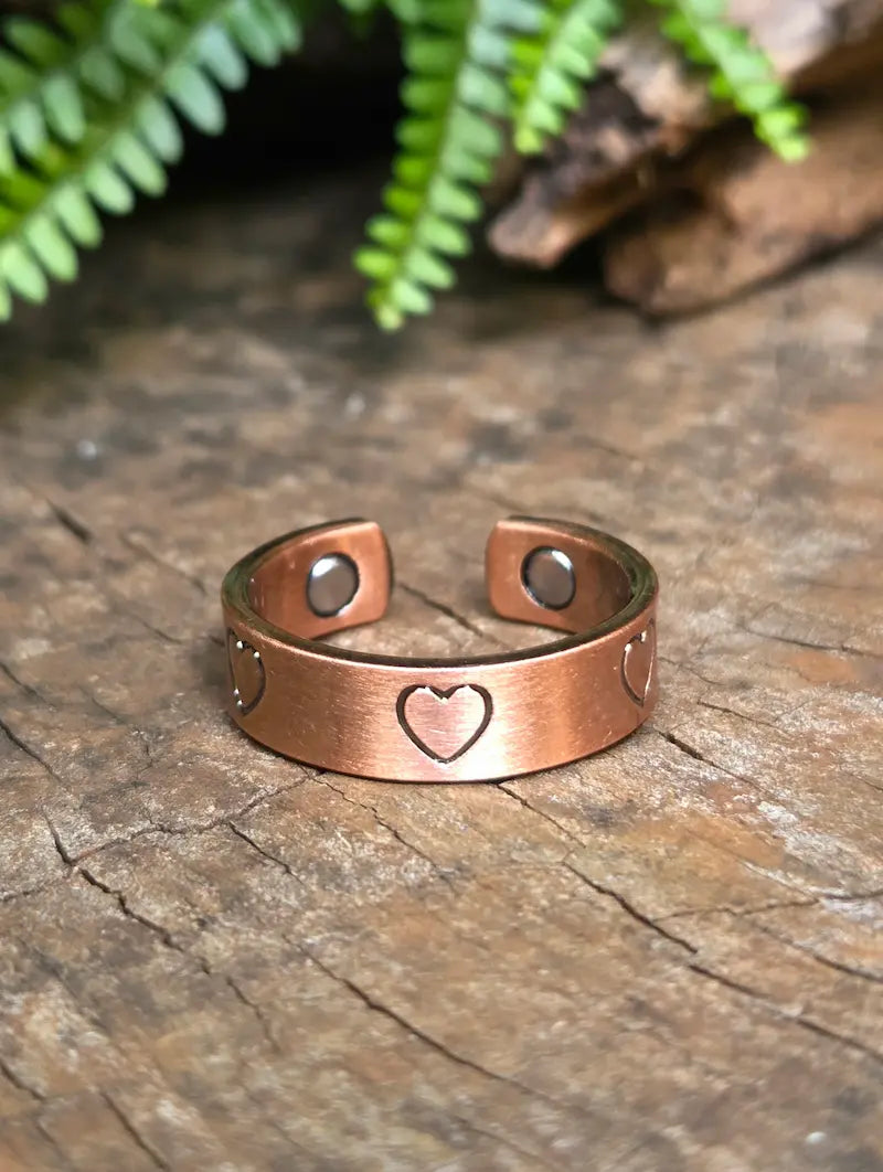 Copper ring with a love heart design on a natural wooden surface with green leaves in the background 