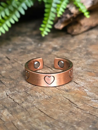 Copper ring with a love heart design on a natural wooden surface with green leaves in the background 