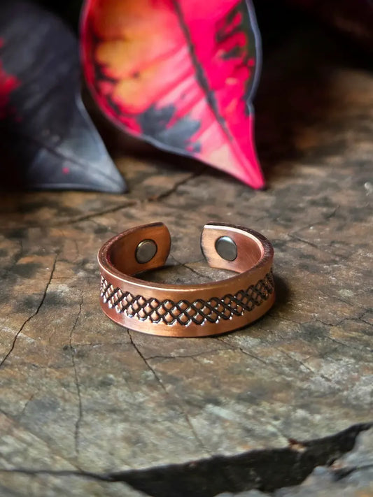 Copper ring with intricate design on a wooden surface with red leaves in the background 