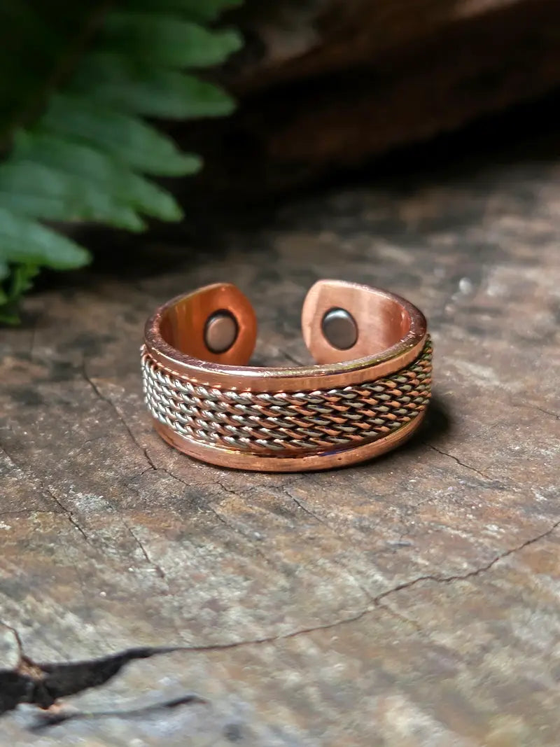 Copper ring on a natural wooden surface with green leaves in the background