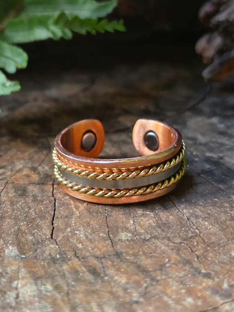 Copper ring resting on a wooden surface with green ferns in the background.