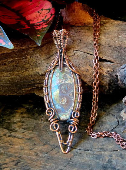 Copper-wrapped pendant with an oval stone on a wooden surface