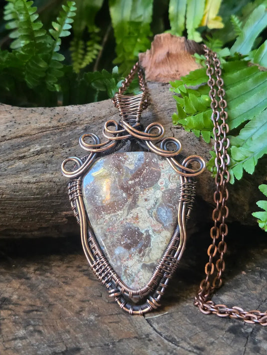 Necklace with a stone pendant on a wooden surface with ferns in the background