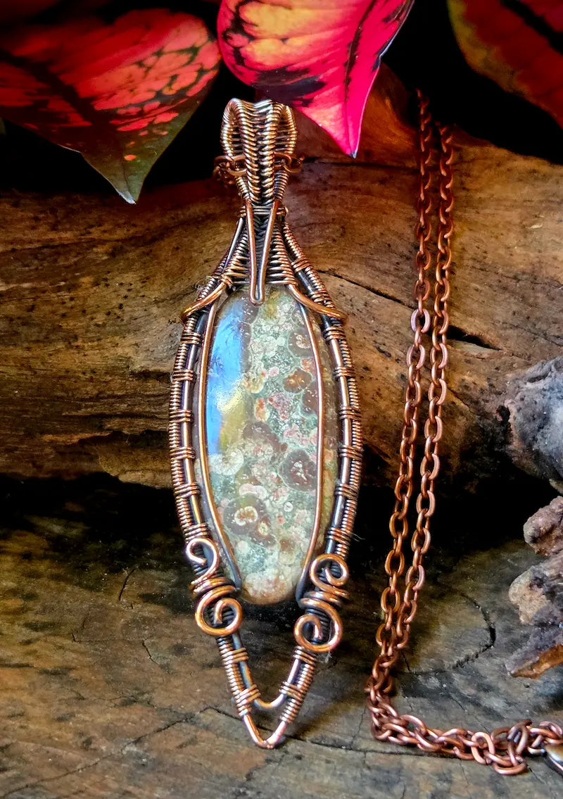 Copper-wrapped pendant with a natural stone on a wooden surface