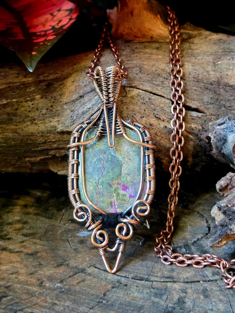 Copper wire-wrapped pendant with a natural stone on a wooden surface