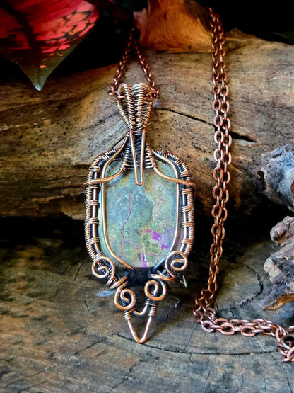 Copper wire-wrapped pendant with a natural stone on a wooden surface