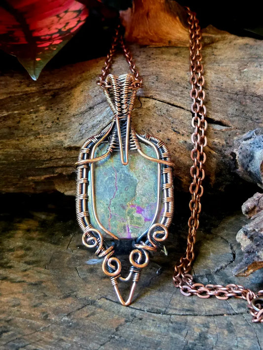 Copper wire-wrapped pendant with a natural stone on a wooden surface