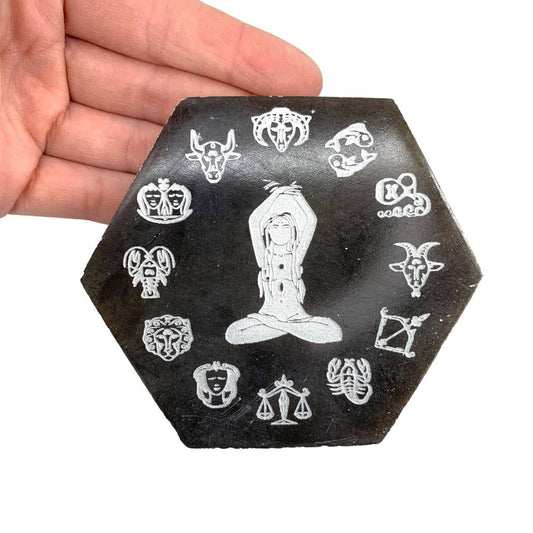 Hexagonal black selenite stone with white zodiac symbol designs held in a hand against a white background