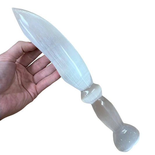 Selenite crystal dagger held in a hand against a white background