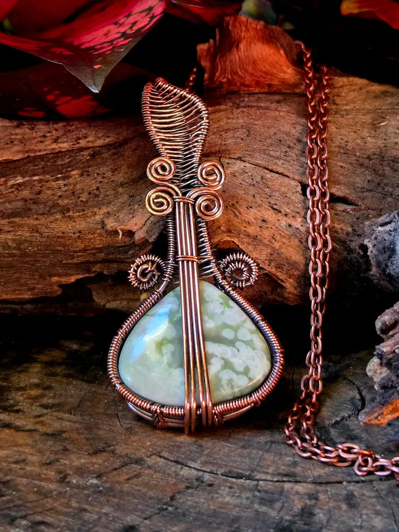 Copper wire-wrapped pendant with a green stone on a wooden surface