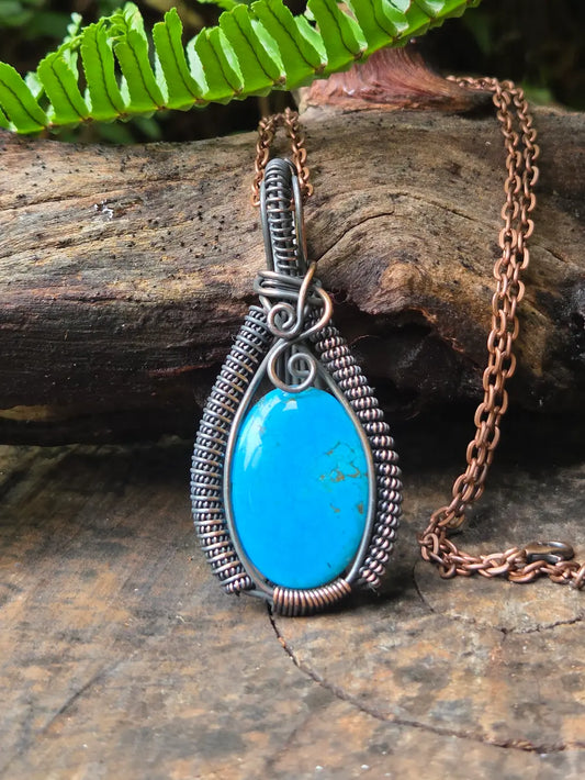 Blue pendant necklace on a wooden surface with green leaves