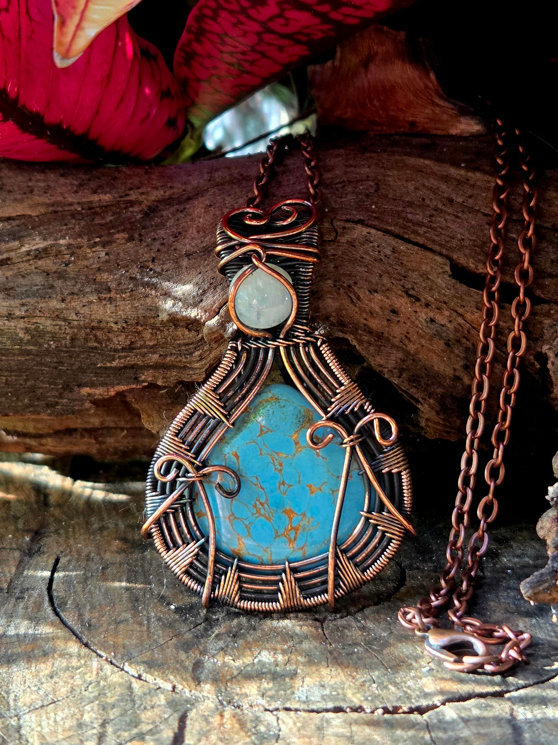 Copper pendant necklace on a natural wooden surface with red leaves in the background 