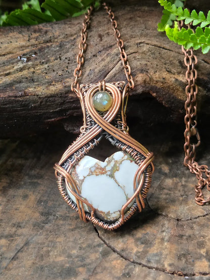 Necklace with a copper wire-wrapped pendant featuring a natural stone on a wooden surface.