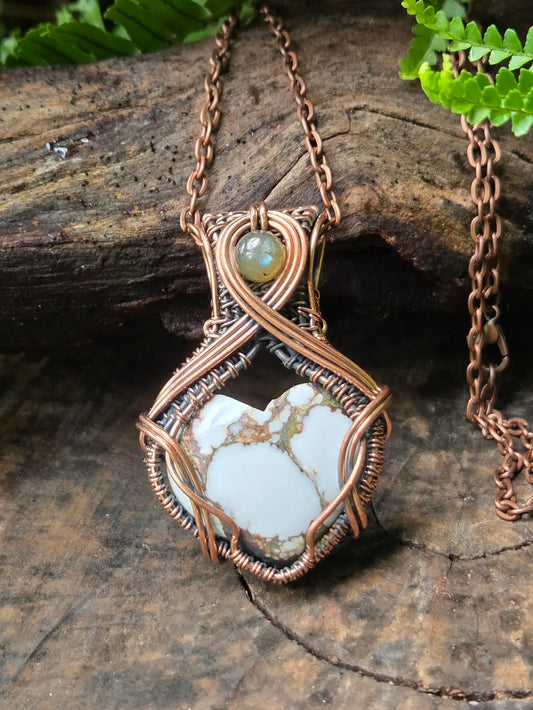 Necklace with a copper wire-wrapped pendant featuring a natural stone on a wooden surface.