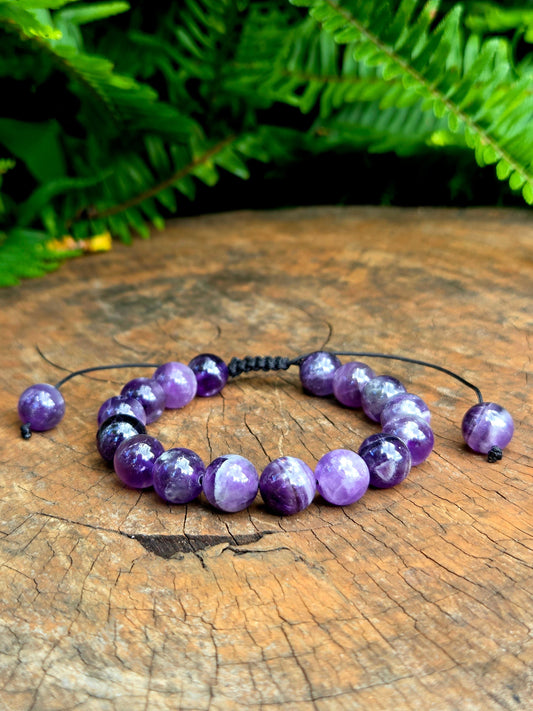 Purple beaded bracelet on a wooden surface with green foliage in the background