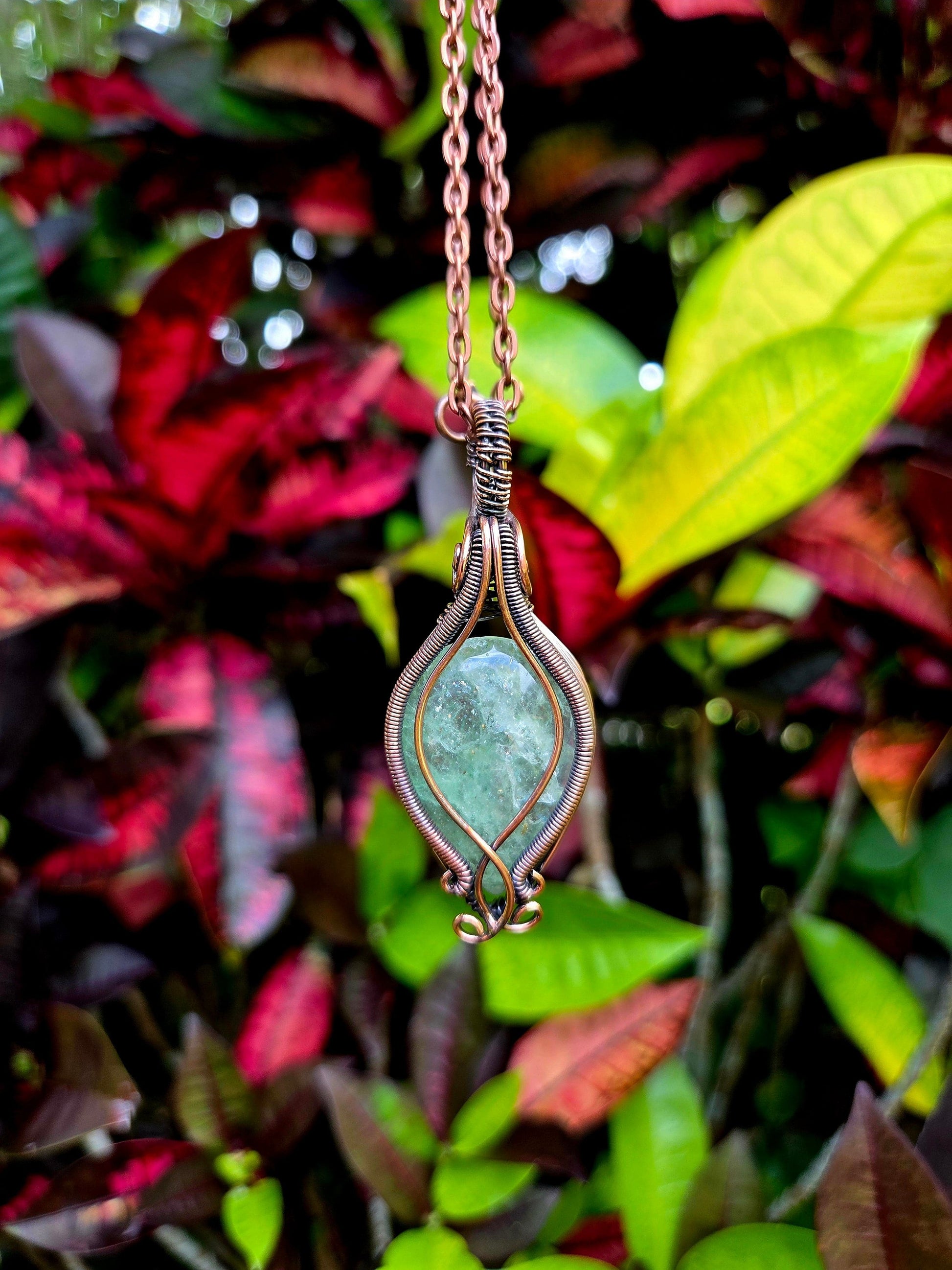 Necklace with a green pendant against a colorful leafy background