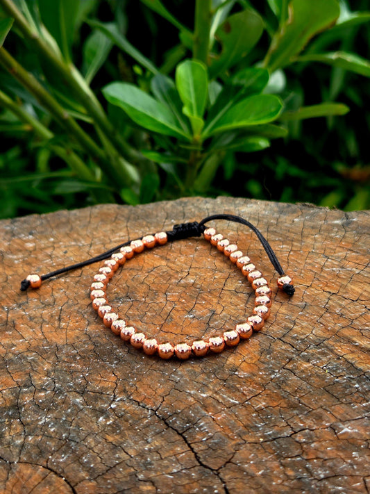Bracelet with rose gold beads on a wooden surface with green leaves in the background