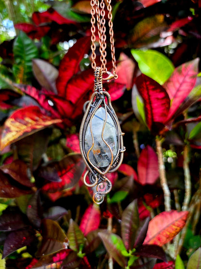 Necklace with a decorative pendant against a background of red and green leaves
