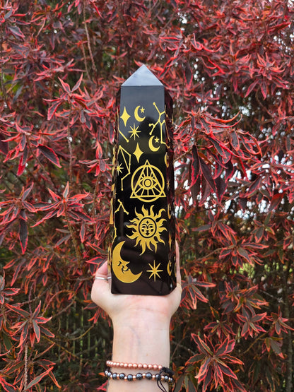 Hand holding a black obsidian crystal with yellow symbols against a red leafy background