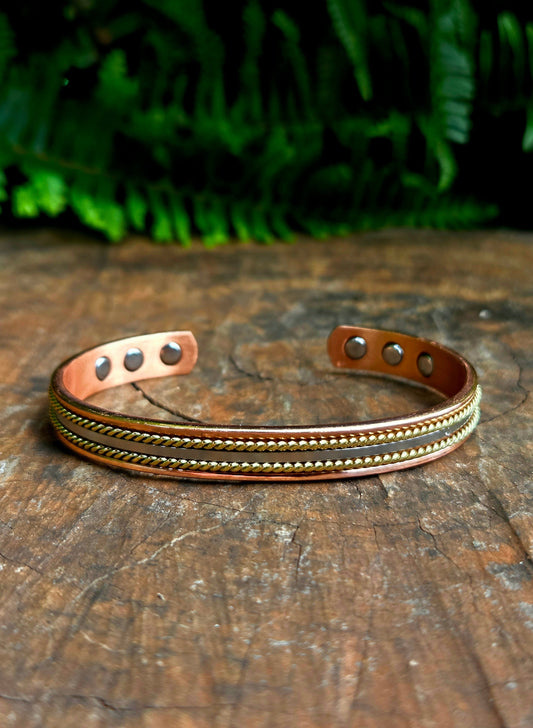 Copper bracelet with embedded stones on a wooden surface with green foliage in the background
