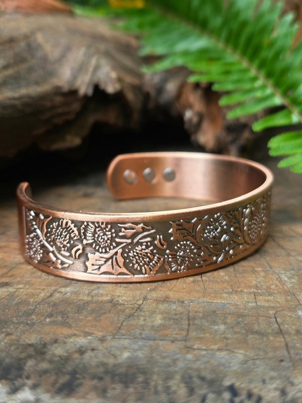 Copper bracelet with floral patterns on a wooden surface with ferns in the background